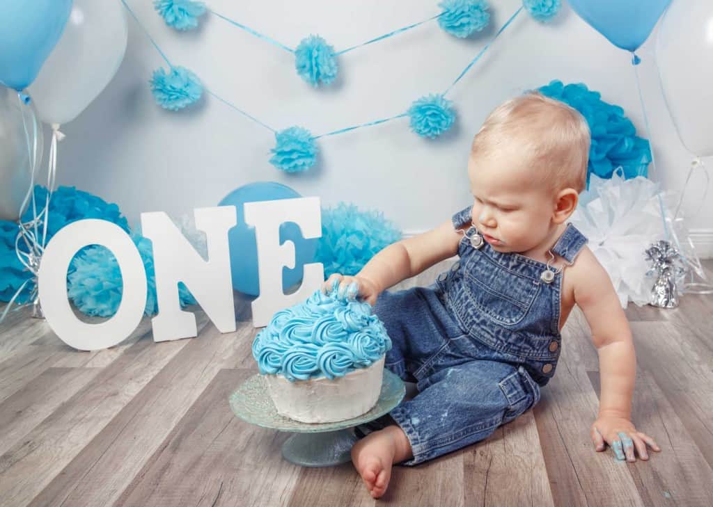 Little boy smashing his first birthday cake with the word one and blue and white decorations
