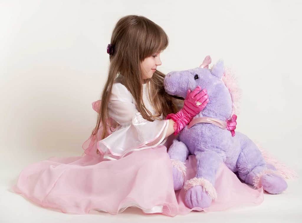 little girl in pink dress hugging a purple stuffed unicorn