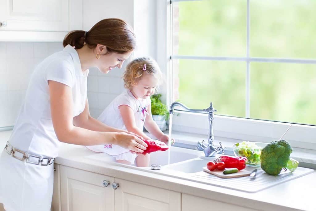 toddler helping mom rinse vegetables in sink