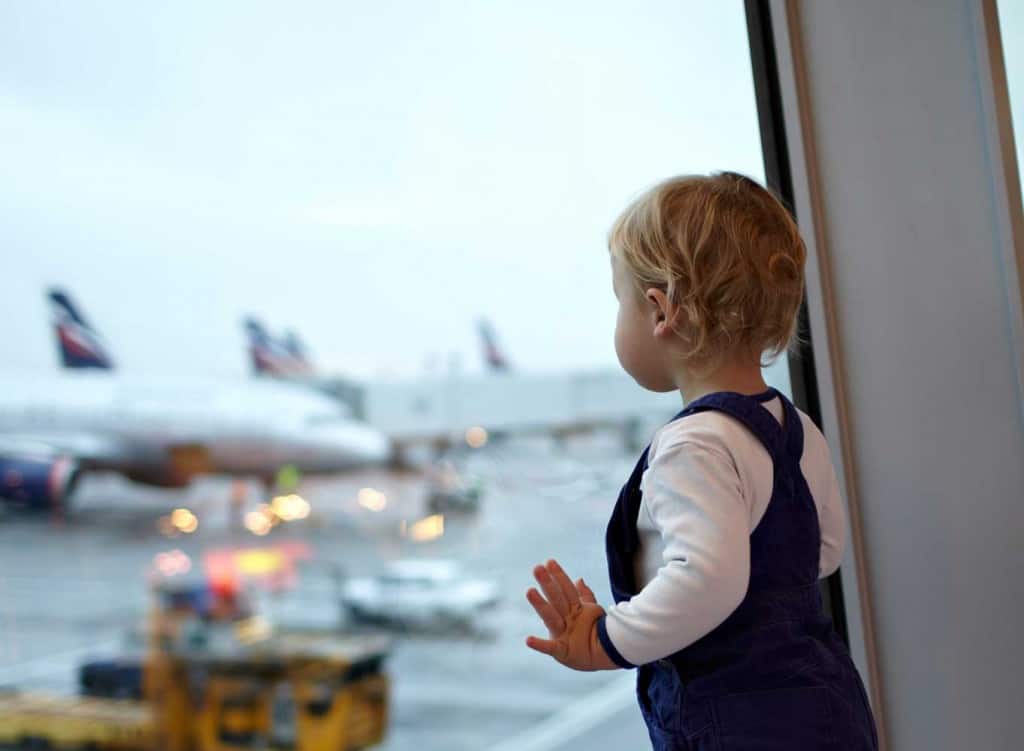 toddler looking out airport window at planes