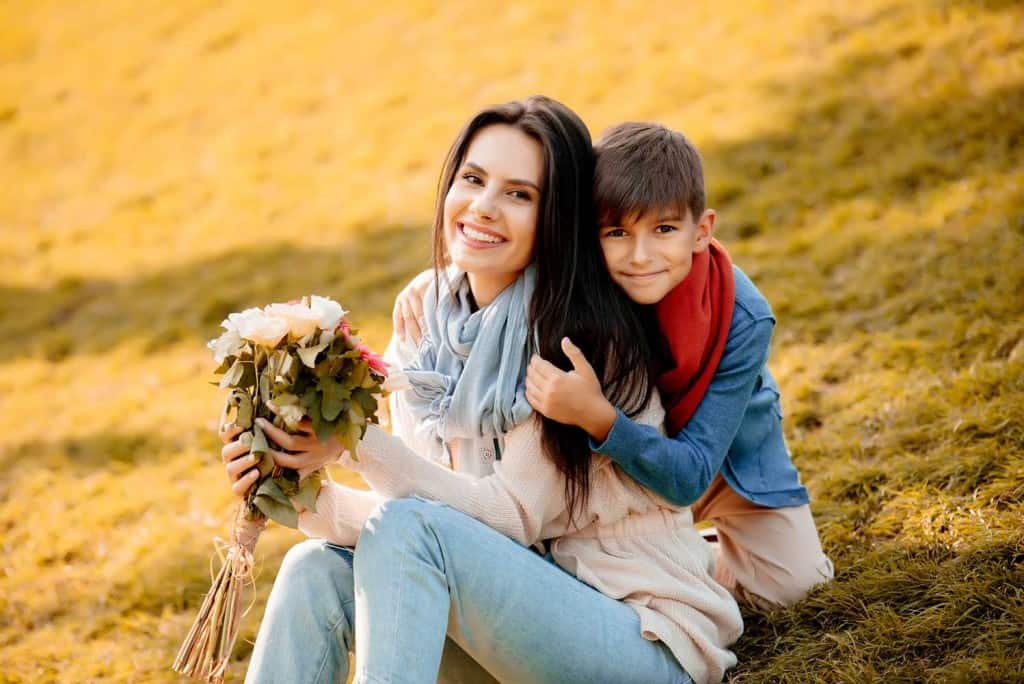 son hugging mom who is holding flowers