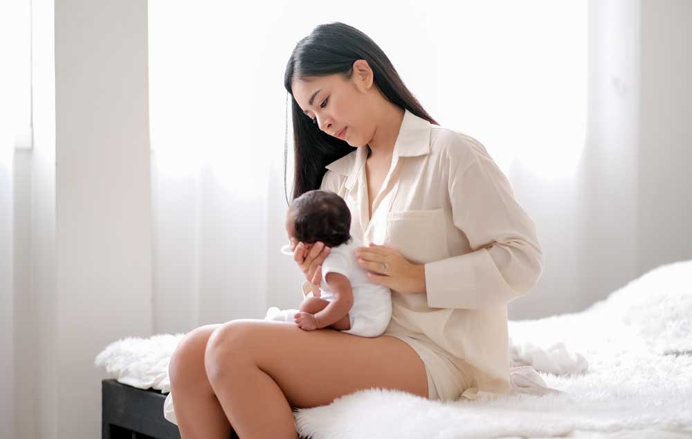 new mom holding baby while using postpartum care kit essentials