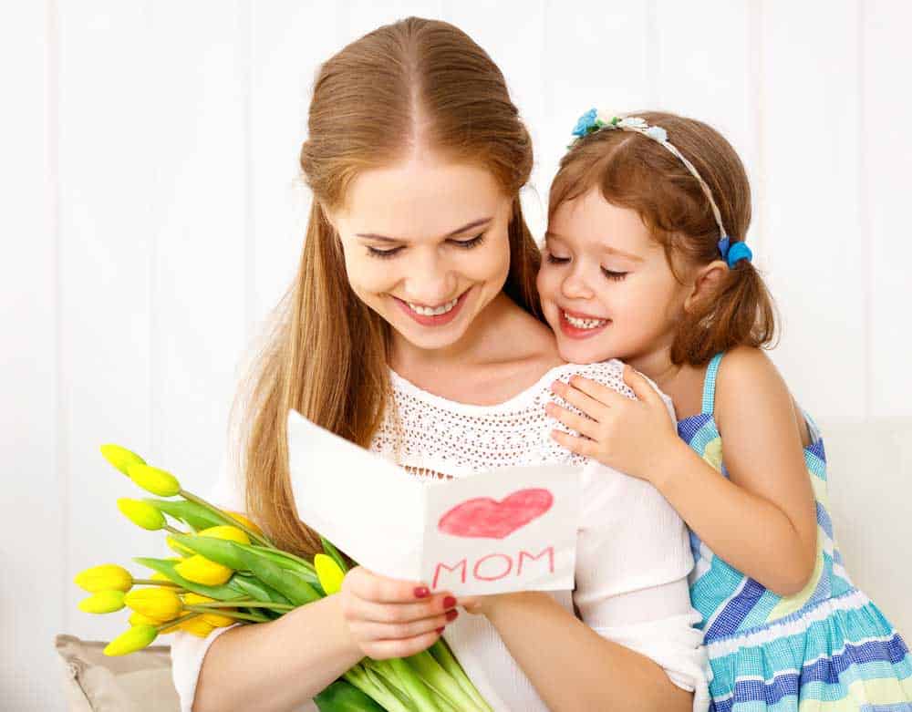 daughter giving mom a homemade mother's day card and flowers